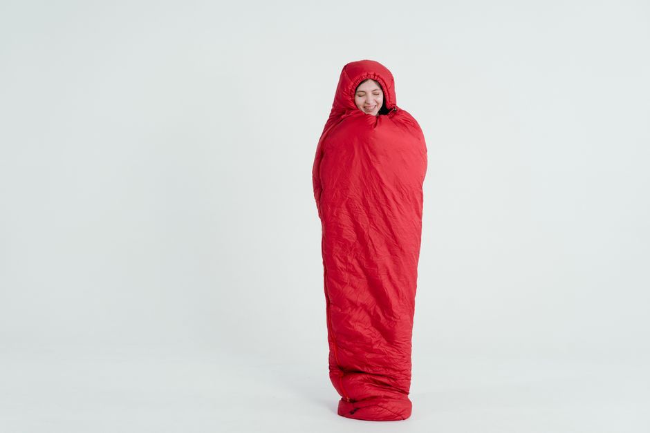 A young woman wrapped in a red sleeping bag, smiling with a serene expression.